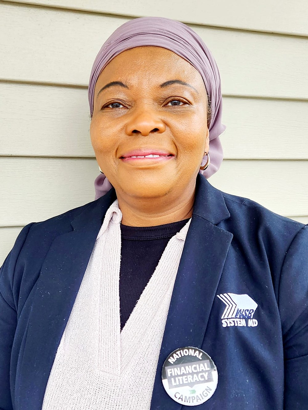 Rashidatu Nyei, licensed financial advisor, standing outdoors in a navy blazer with a National Financial Literacy Campaign pin